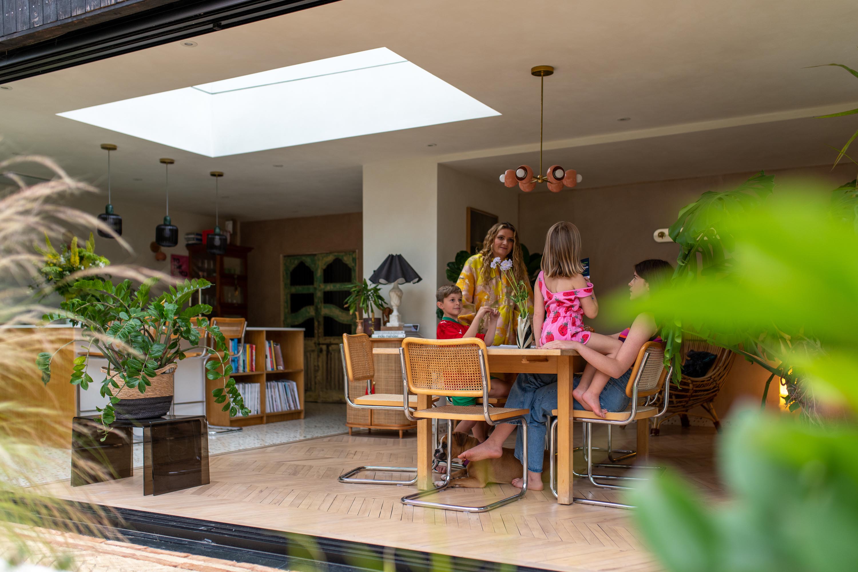 exterior view looking into the kitchen and dining extension. Custom Roof window above, letting a lot of natural light into the space. Family seated around dining table 