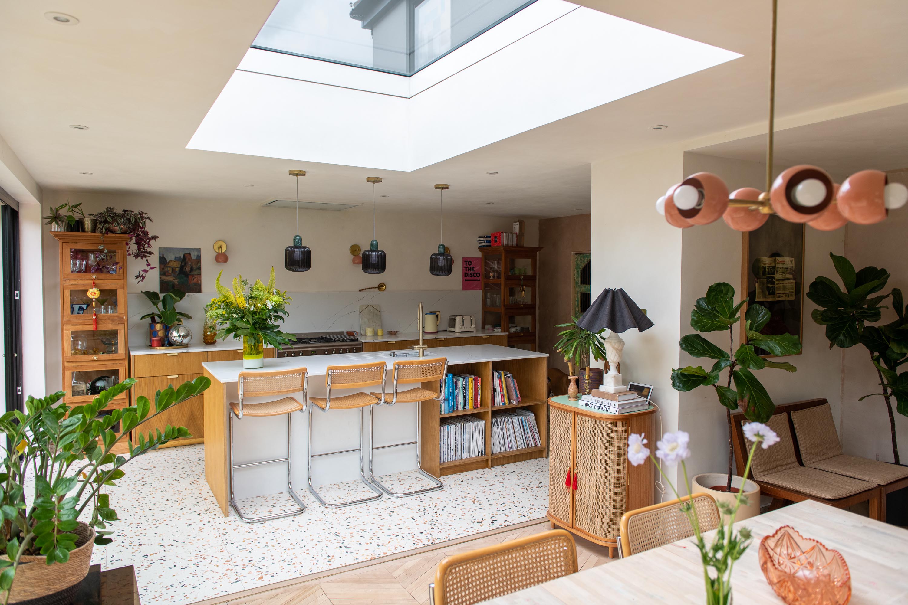 wide shot of kitchen and dining extension. Skylight above, lots of earthy tones and plants used 