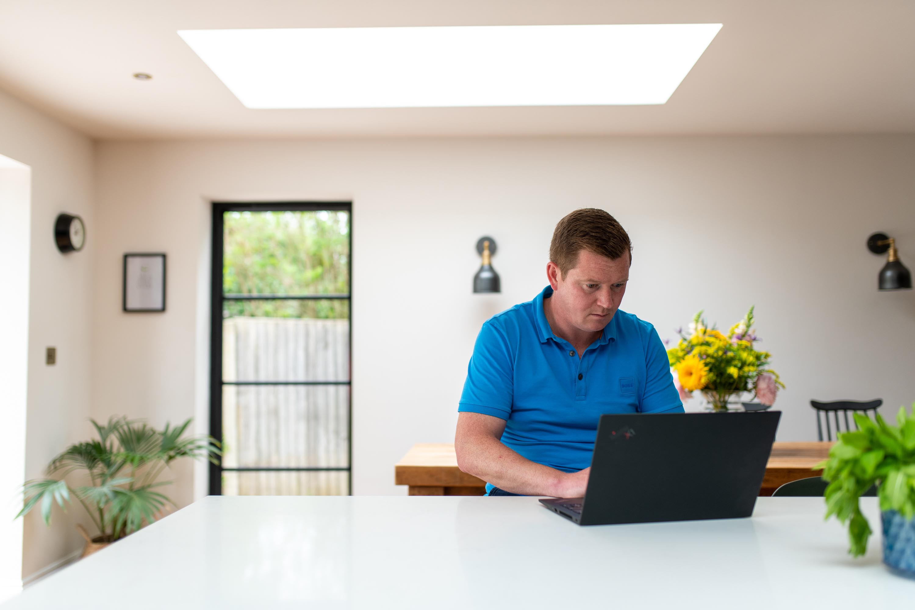 Man working on laptop in kitchen extension under a rooflight 
