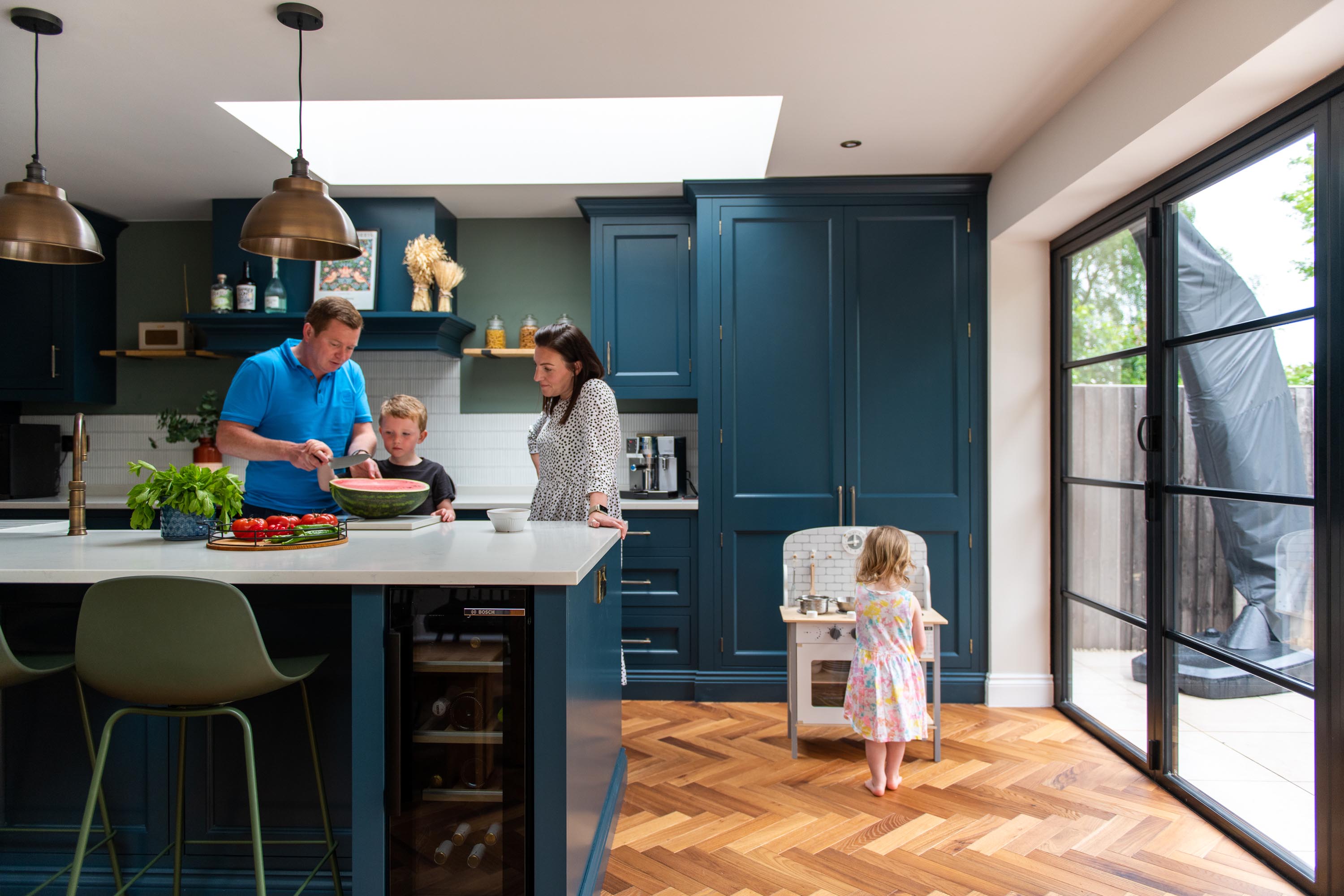 family of four around kitchen island playing and eating, rooflight above